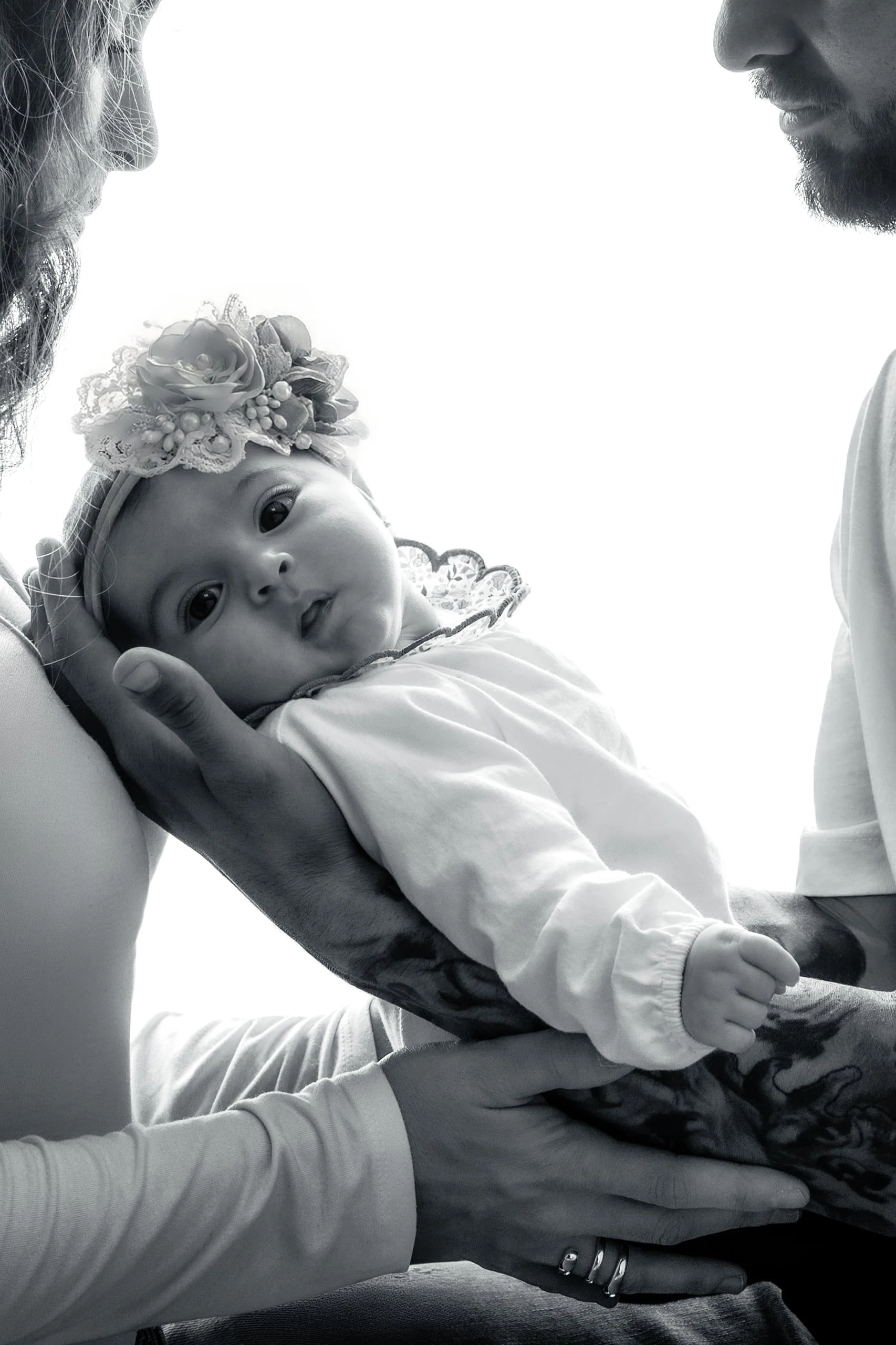Bebé recién nacido sostenido por sus padres en blanco y negro.
