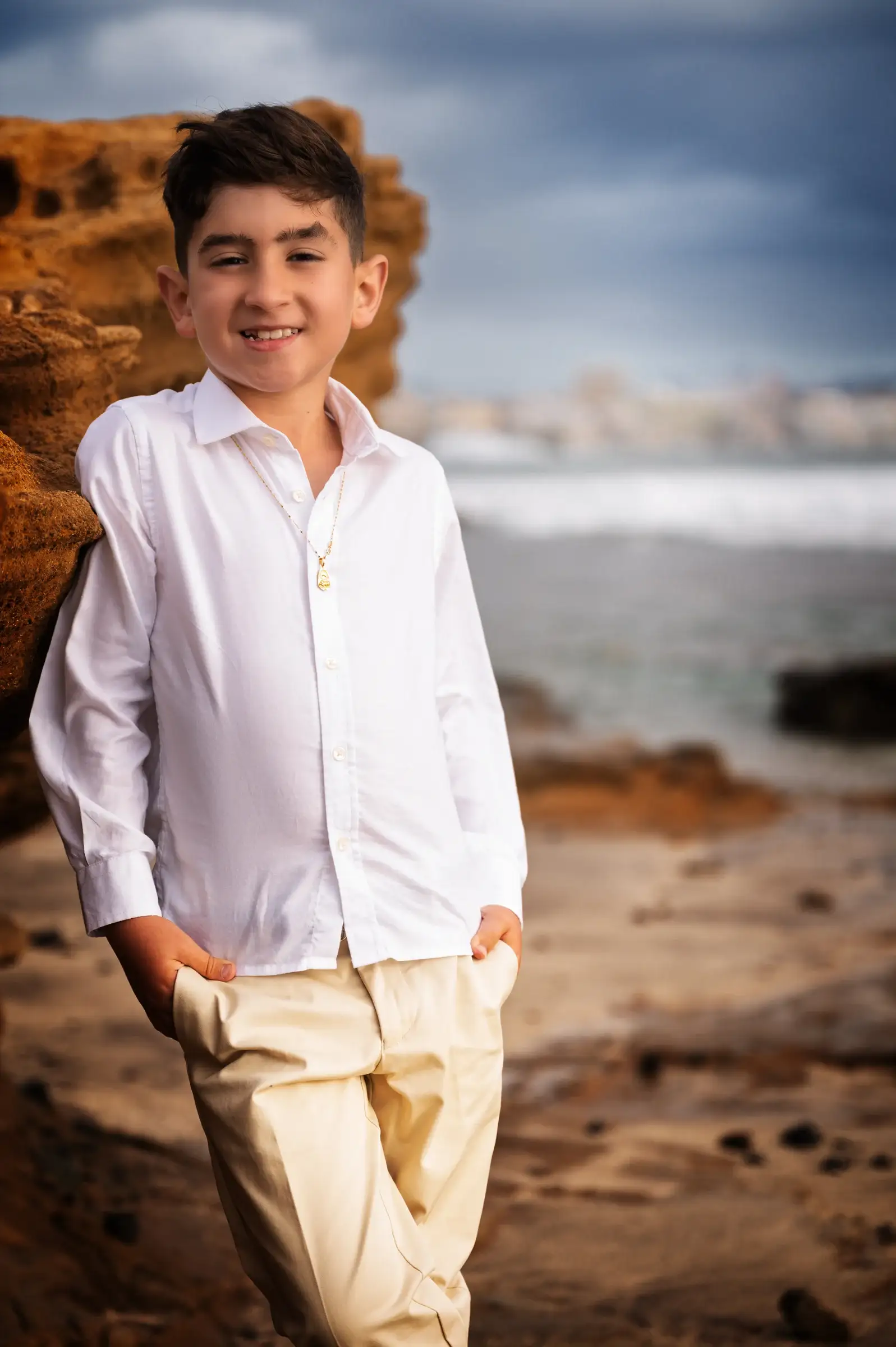 Niño con camisa blanca sonriendo junto al mar.